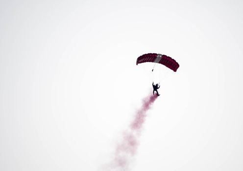 silhouette parachute stunt unfocused and blurry while gliding in the air with red smoke trail during an air exhibition in Singapore