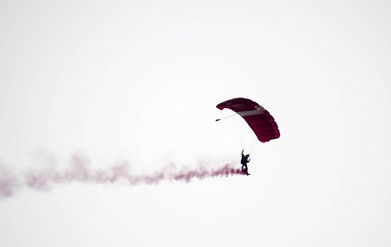 silhouette parachute stunt unfocused and blurry while gliding in the air with red smoke trail during an air exhibition in Singapore