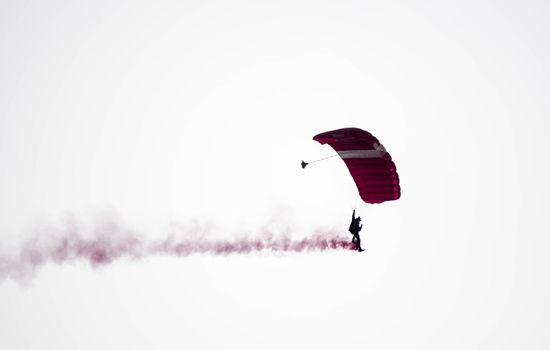 silhouette parachute stunt unfocused and blurry while gliding in the air with red smoke trail during an air exhibition in Singapore