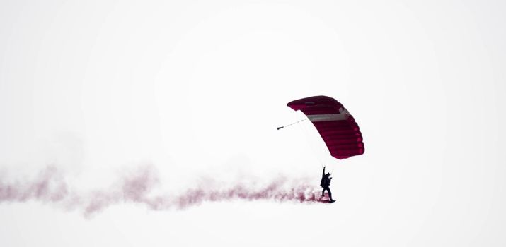 silhouette parachute stunt unfocused and blurry while gliding in the air with red smoke trail during an air exhibition in Singapore