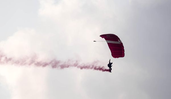 silhouette parachute stunt unfocused and blurry while gliding in the air with red smoke trail during an air exhibition in Singapore