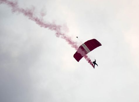 silhouette parachute stunt unfocused and blurry while gliding in the air with red smoke trail during an air exhibition in Singapore