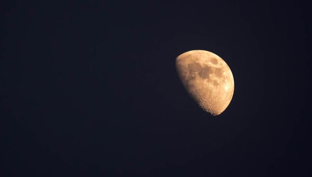 Extreme zoom tele photo of yellow half moon as seen during night on a clear sky.