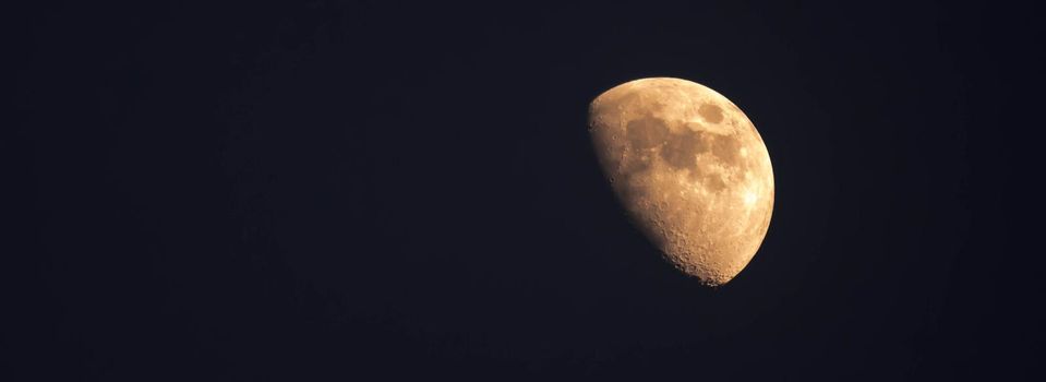 Extreme zoom tele photo of yellow half moon as seen during night on a clear sky.