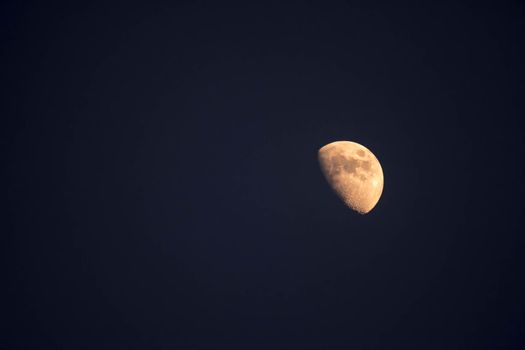 Extreme zoom tele photo of yellow half moon as seen during night on a clear sky.