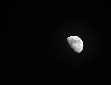 Extreme zoom tele photo of yellow half moon as seen at night on a clear sky.