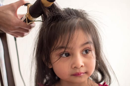 Stylist curling hair for little girl in a parlor. Pretty little girl with curly hair and make up