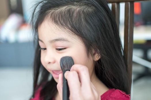Pretty cute little girl while having a makeup, lipstick and blush on