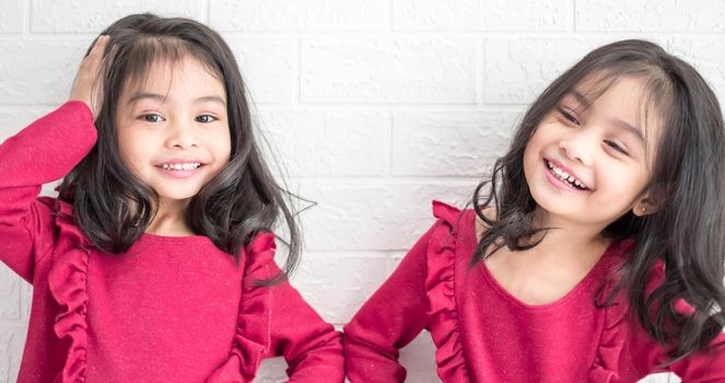 An Identical twin girls sisters are posing for the camera. Happy twin sisters in dresses are looking at the camera and smiling. Frontal view, on white background