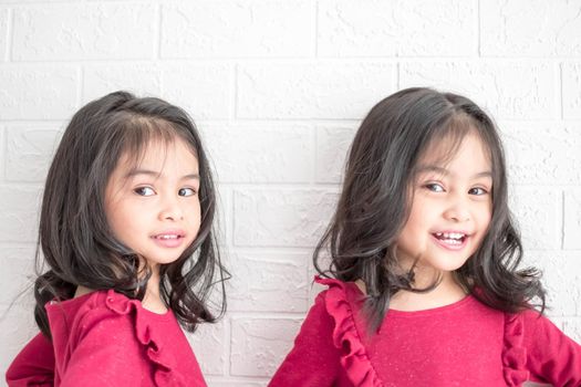 An Identical twin girls sisters are posing for the camera. Happy twin sisters in dresses are looking at the camera and smiling. Frontal view, on white background