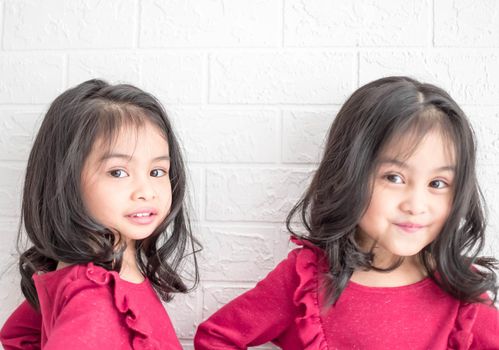 An Identical twin girls sisters are posing for the camera. Happy twin sisters in dresses are looking at the camera and smiling. Frontal view, on white background