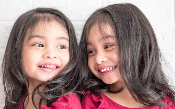 An Identical twin girls sisters are posing for the camera. Happy twin sisters in dresses are looking at the camera and smiling. Frontal view, on white background