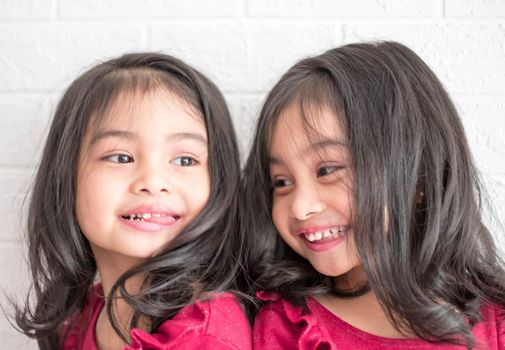 An Identical twin girls sisters are posing for the camera. Happy twin sisters in dresses are looking at the camera and smiling. Frontal view, on white background