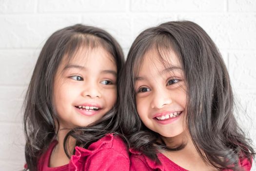 An Identical twin girls sisters are posing for the camera. Happy twin sisters in dresses are looking at the camera and smiling. Frontal view, on white background