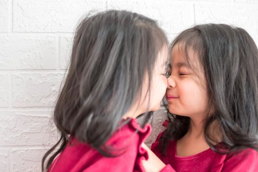 Pretty little girl twins having fun and kissing each other on White background