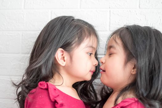 Pretty little girl twins having fun and kissing each other on White background