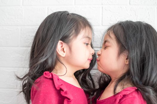 Pretty little girl twins having fun and kissing each other on White background