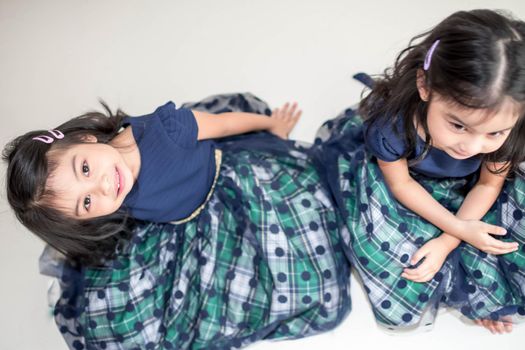 An Identical twin girls sisters are posing for the camera. Happy twin sisters in dresses are looking at the camera and smiling. Frontal view, on white background