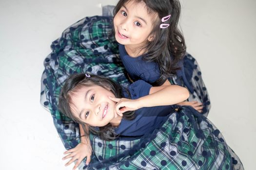 An Identical twin girls sisters are posing for the camera. Happy twin sisters in dresses are looking at the camera and smiling. Frontal view, on white background