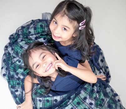 An Identical twin girls sisters are posing for the camera. Happy twin sisters in dresses are looking at the camera and smiling. Frontal view, on white background