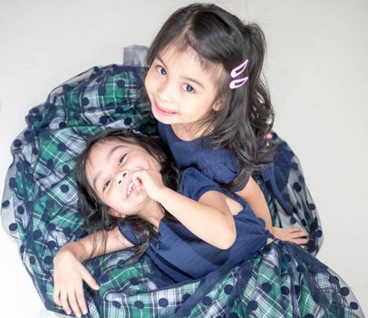 An Identical twin girls sisters are posing for the camera. Happy twin sisters in dresses are looking at the camera and smiling. Frontal view, on white background