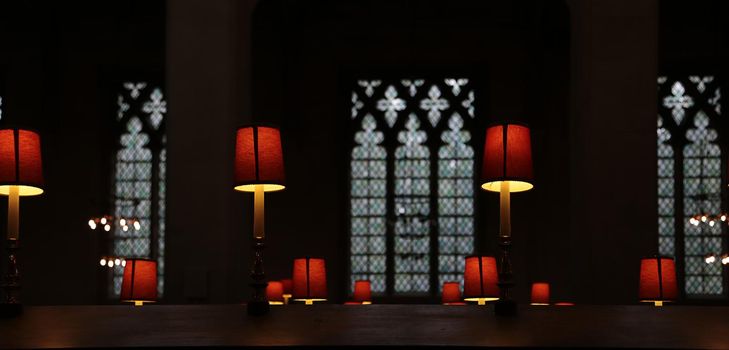 Calm empty dark church with mystic lights. Old Christian Church cathedral interior with red lamps and light through gothic arc windows in soft focus