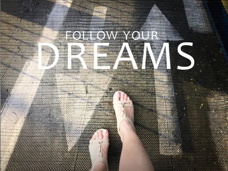 Follow your dreams word with arrow on road and woman feet background