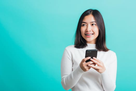 Portrait of Asian woman smile she holding and typing text message on a smartphone, female excited cheerful her reading mobile phone some social media isolated on a blue background, Technology concept