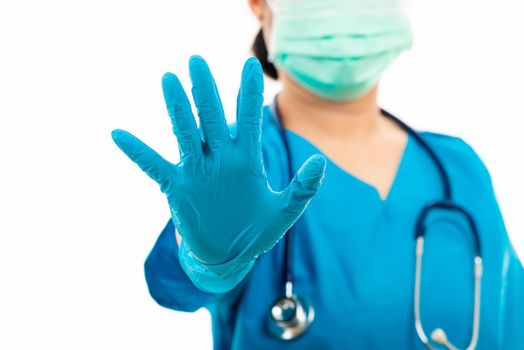 Female nurse with stethoscope puts rubber gloves and wearing medical face mask, woman doctor in blue uniform show hand up stop sign, studio shot isolated over white background, medical health concept