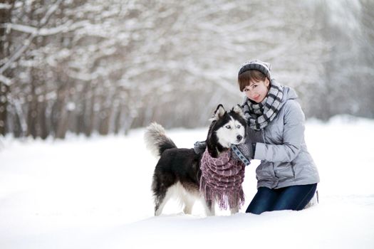 The Girl sitting in the snow with a siberian husky dog in the winter forest