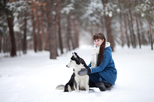 The Girl sitting in the snow with a siberian husky dog in the winter forest