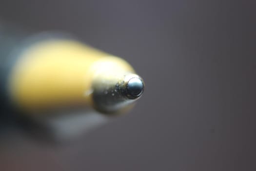 Macro photo of ballpoint pen tip with dark grey background. Extreme macro image of metal ballpoint pen on grey background.