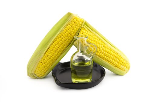 Corn oil in decanter in the cast iron skillet and fresh corncobs next to the cast iron skillet isolated on white background with free copy space for text