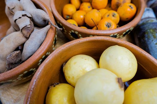 Fresh yellow guavas, Mexican hawthorns, and tamarind in handmade clay bowls. Close-up of brown bowls of Mexican fruit. Traditional snack preparation