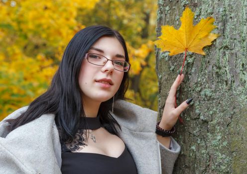 young girl holding a yellow maple leaf in her hand in the park in autumn. portrait closeup