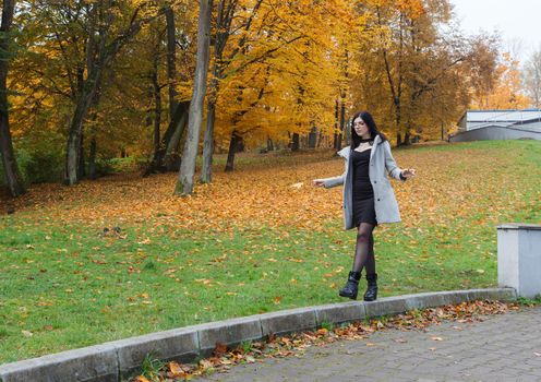 young girl in a gray coat walking on an alley in a city park on an autumn day