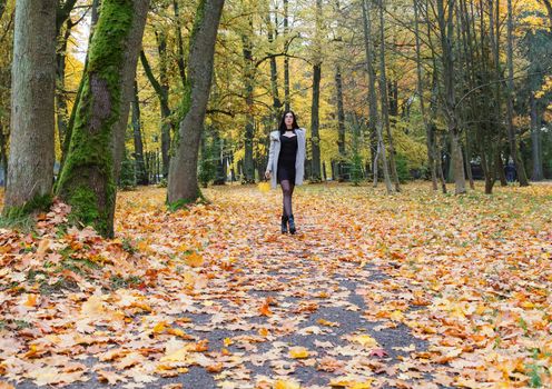 young girl in a gray coat walking on an alley in a city park on an autumn day