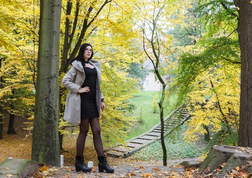 young girl in a gray coat stands on an alley in a city park on an autumn day