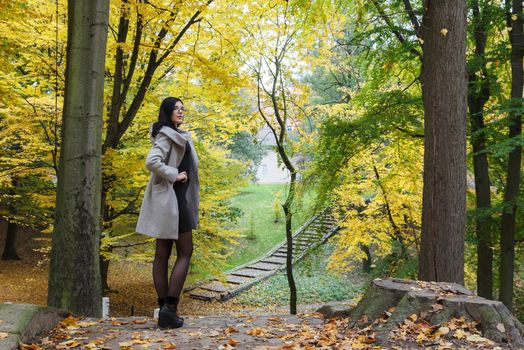 young girl in a gray coat stands on an alley in a city park on an autumn day