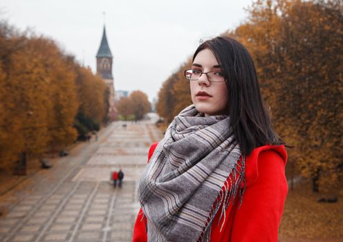 portrait of young girl in a red coat standing on the alley of the park on an autumn day