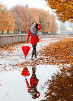 young girl in a red coat with an umbrella stands on the alley of the park after the rain on gloomy autumn day