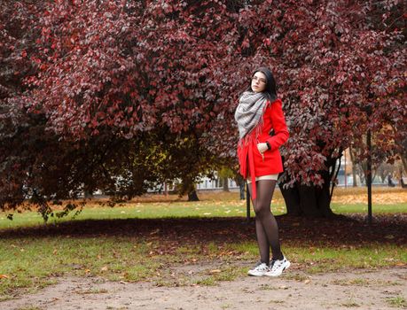 young girl in a red coat standing on the alley of a city park on a autumn day