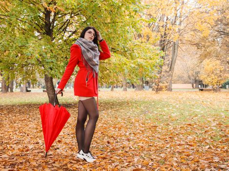 young girl in a red coat with an umbrella standing on the alley of a city park on a sunny autumn day