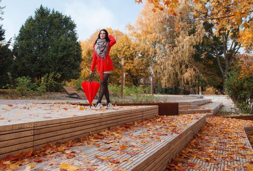 young girl in a red coat with an umbrella standing on the alley of a city park on a sunny autumn day