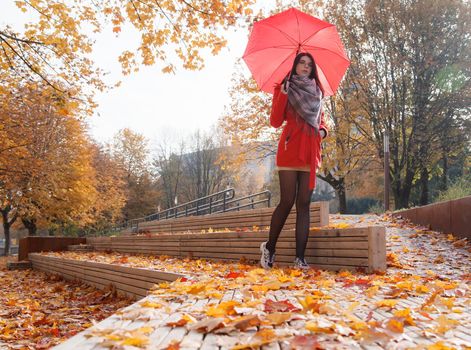 young girl in a red coat with an umbrella standing on the alley of a city park on a sunny autumn day