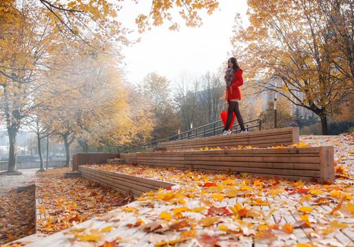 young girl in a red coat with an umbrella standing on the alley of a city park on a sunny autumn day