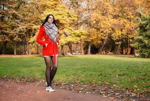 young beautiful girl in a red coat standing on the alley of a city park on a sunny autumn day