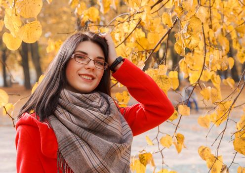 portrait of young smiling girl in a red coat standing on the alley of the park on an autumn day