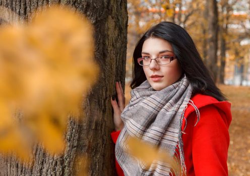 portrait of young girl in a red coat standing on the alley of the park on an autumn day