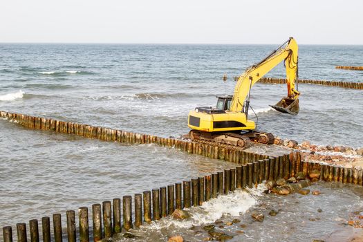 excavator during the construction of a breakwater by the sea on autumn day